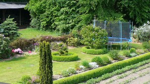 A well-maintained garden with neatly trimmed hedges, a variety of flowering plants, and a trampoline.