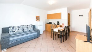 Un espace de vie compact comprenant un canapé, une table à manger, des chaises, un coin cuisine et un téléviseur.