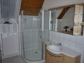 Un baño moderno con cabina de ducha de vidrio, lavamanos blanco y tocador de madera.