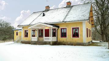 Ein gelbes Haus mit weißer Veranda und roten Fenstern, umgeben von Schnee.