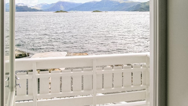 A view from a balcony with a railing, overlooking a body of water with distant mountains.