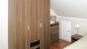 A bedroom with a wooden wardrobe, a dresser, a bedside table, and a lamp.