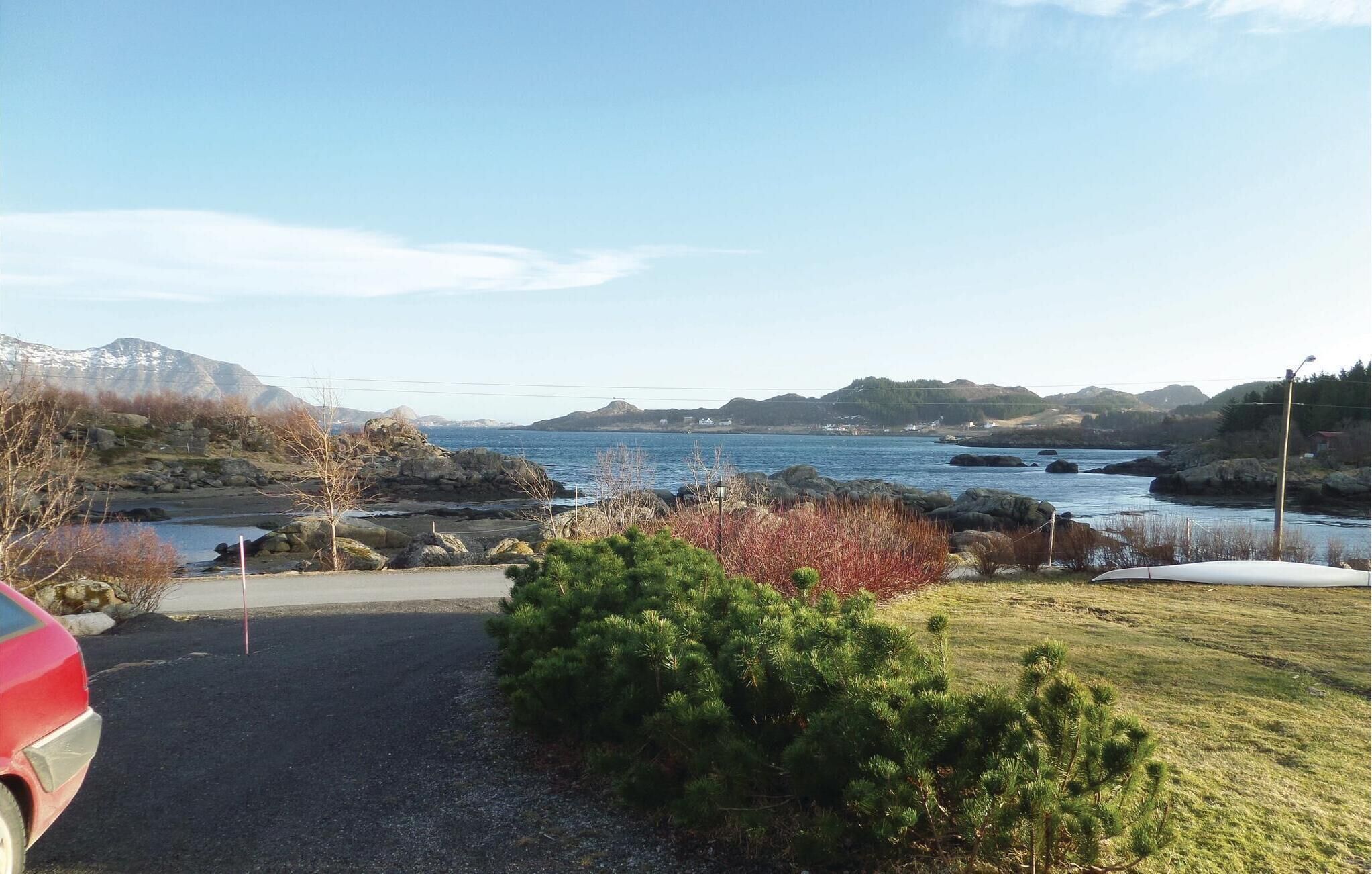 A coastal landscape with a gravel path, a parked red car, and a small green bush.