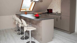 A modern kitchen with a central island, bar stools, a stainless steel range hood, and a refrigerator. - Apartment Lischewski - Volker Lischewski (Steinberg)