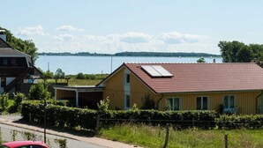 A yellow house with a red roof, a covered porch, and a view of a lake. - Apartment Lischewski - Volker Lischewski (Steinberg)