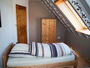 Quarto pequeno com teto inclinado e claraboia, guarda-roupa de madeira e cama com roupa de cama listrada.