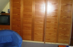 Een kamer met een houten garderobe, een televisie op een standaard en een blauwe stoel.