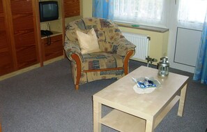 Een woonkamer met een gestreept fauteuil, een houten salontafel, een tafeltje met een lantaarn en een radiator.