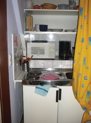 Een kleine keuken met een magnetron, koffiezetapparaat en een fornuis.