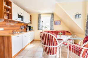 A compact kitchen with white cabinets, a microwave, and a wooden countertop. There is a dining area with a glass table and wicker chairs.