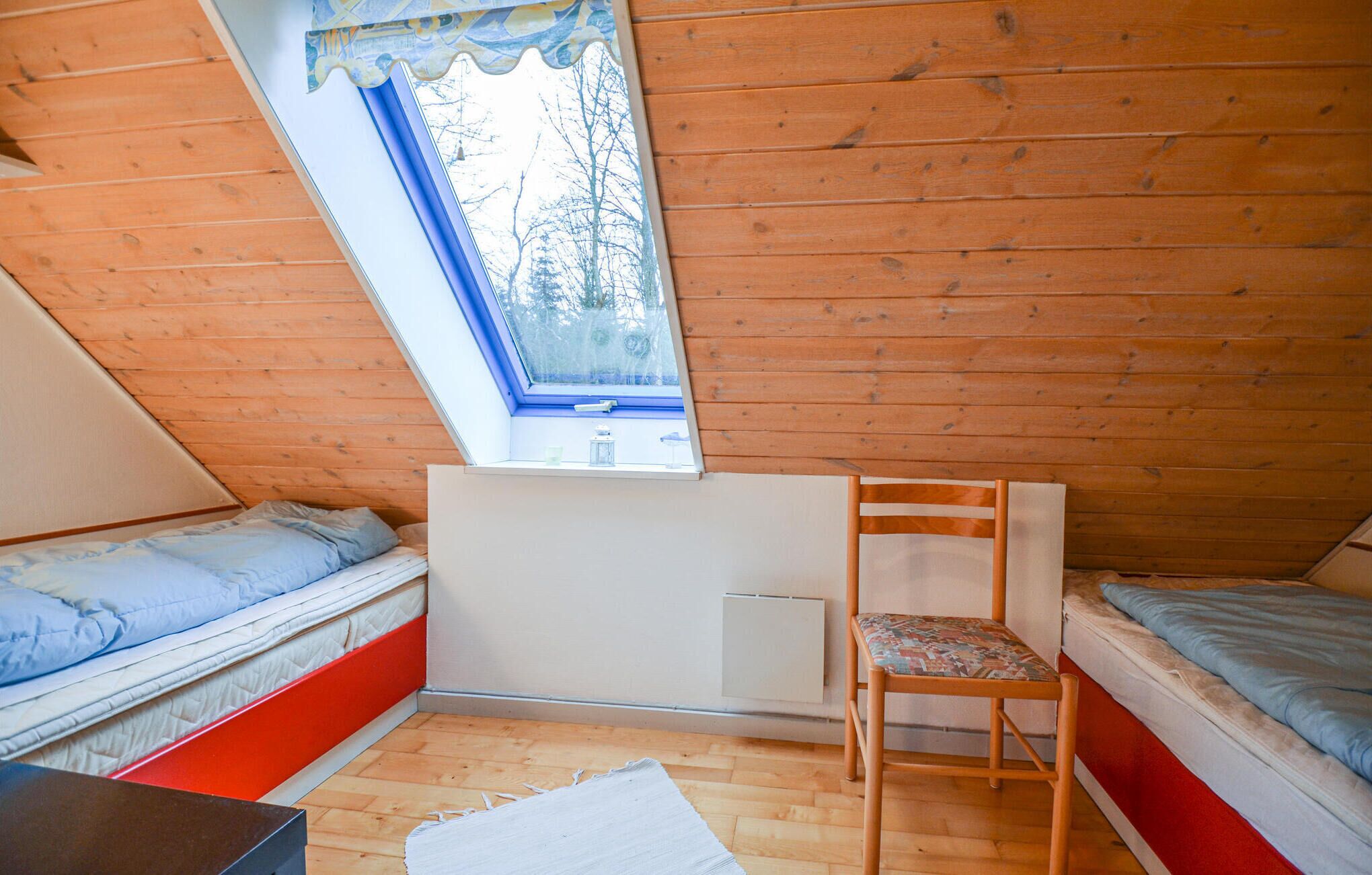 Ein kleiner Raum mit niedrigem Pultdach, zwei Betten, einem Sessel und einem Fenster.