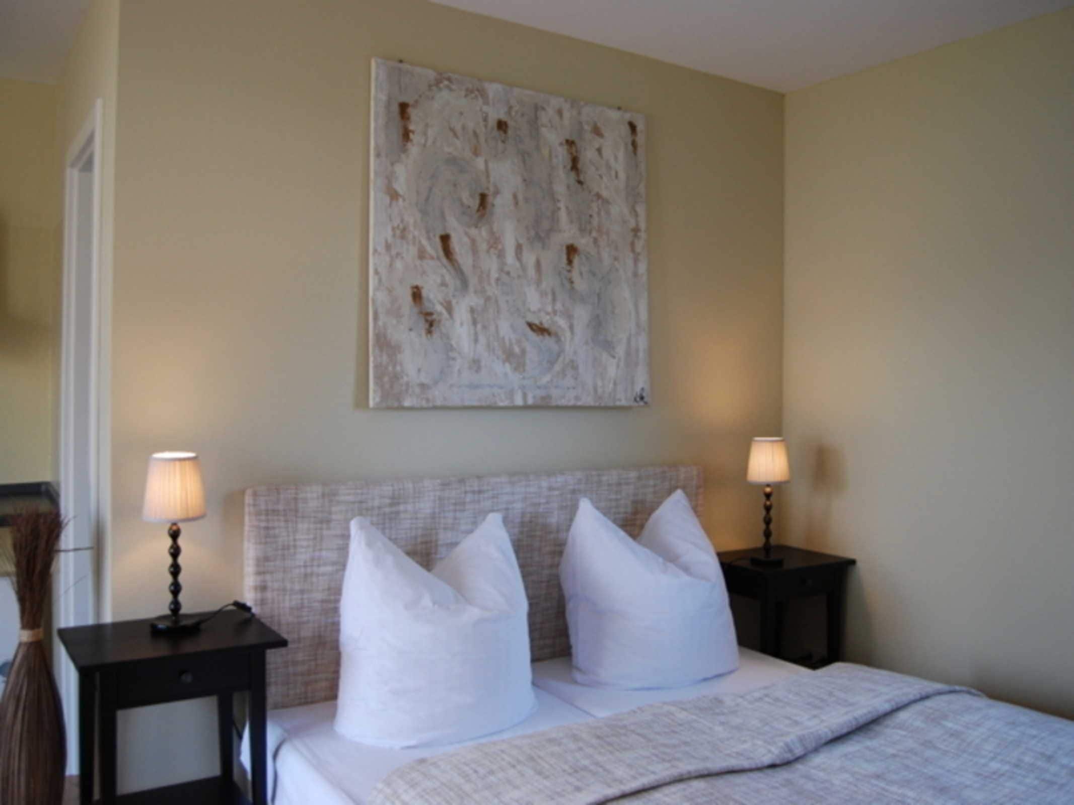 Une chambre d’hôtel avec un lit, deux tables de chevet, deux lampes et un grand tableau abstrait accroché au mur.