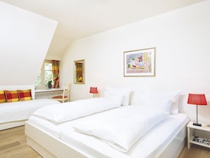 Une chambre d’hôtel avec deux lits, un bureau, une chaise, une lampe rouge et un tableau encadré au mur.
