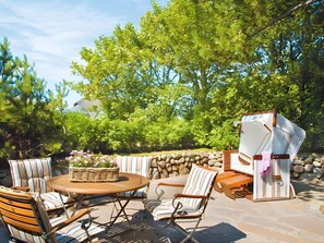 Une terrasse extérieure avec une table ronde en bois, des chaises à rayures et un fauteuil en osier sur lequel est posée une serviette.