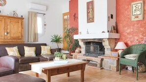 Ein gemütliches Wohnzimmer mit Kamin, einer Sofagarnitur, einem Holzschrank und einem grünen Sessel.