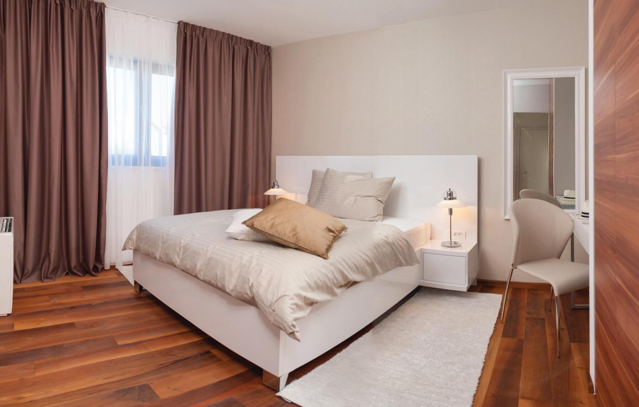 A modern bedroom with a large bed, bedside tables, a chair, and a mirror.