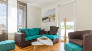 A modern living room with a teal sofa, a brown armchair, and a white coffee table. - Apartment Scholle - CuxDuHier (Cuxhaven)