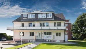 A two-story building with a flat roof, a balcony on the upper floor, and a front entrance with steps. - Apartment Scholle - CuxDuHier (Cuxhaven)