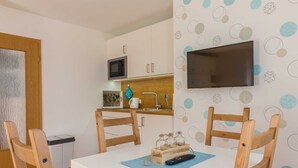 A compact kitchen with white cabinets, a microwave, and a TV mounted on the wall. - Apartment Scholle - CuxDuHier (Cuxhaven)