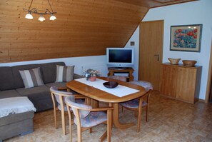 Un salon chaleureux avec un plafond en bois, un téléviseur, une table à manger avec des chaises, un canapé et un meuble contenant des objets décoratifs.