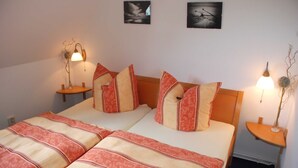Una cama doble con una colcha estampada, dos mesitas de noche con lámparas, y dos cuadros en la pared.