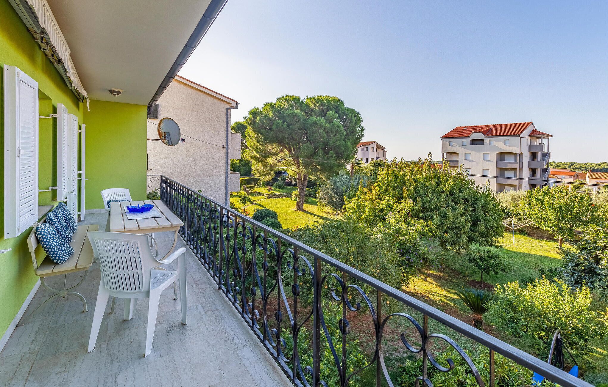 A balcony with a table and chairs, overlooking a garden and buildings.
