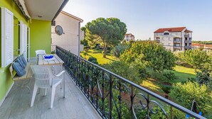 Un balcone con tavolo e sedie, vista su un giardino e degli edifici.