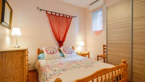 A bedroom with a wooden bed, two bedside lamps, a wooden nightstand, a red net curtain, a wooden wardrobe, and a window with blinds.