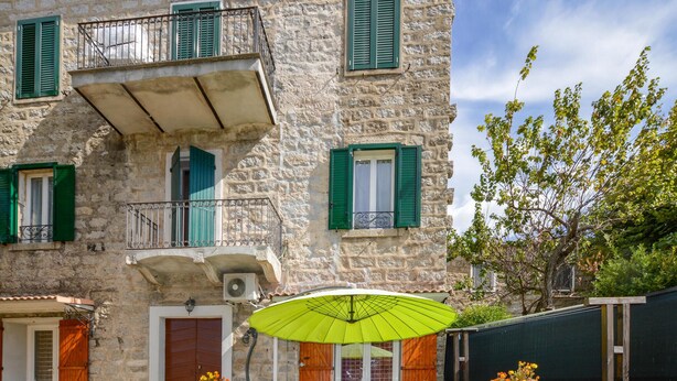 A stone building with green shutters, a balcony, and a wooden door.