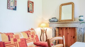 A cozy living room with a patterned sofa, a wooden chair, a table, a radio, a mirror, and a lamp.