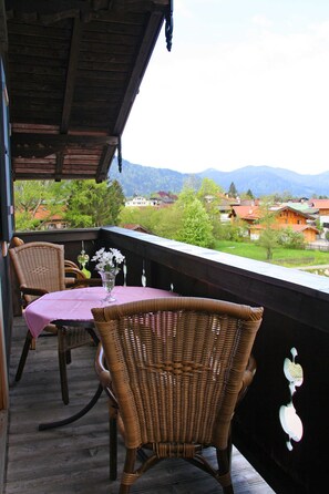 A balcony with wicker chairs and a table, overlooking a village and mountains. - Apartment Rierk - Gästehaus Schiffmann (Tegernsee)