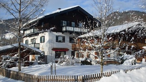 Un edificio de varios pisos con techo cubierto de nieve, balcones de madera y una valla de madera en un paisaje nevado.