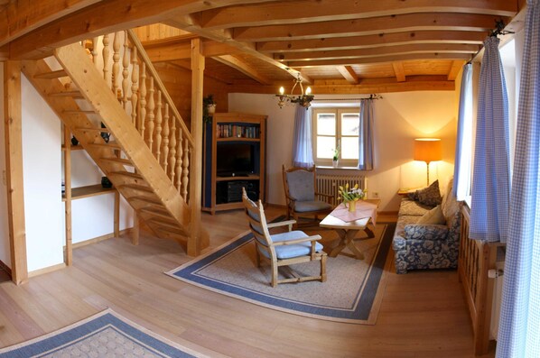 A wooden interior with a staircase, a sofa, a table, and a bookshelf. - Apartment Rierk - Gästehaus Schiffmann (Tegernsee)