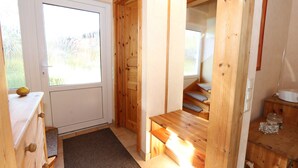 Un interno in legno con una porta, una panca e un piccolo tavolo con un barattolo.