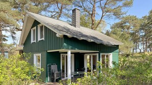 Una casa verde con veranda, camino e una pila di sedie all'esterno.
