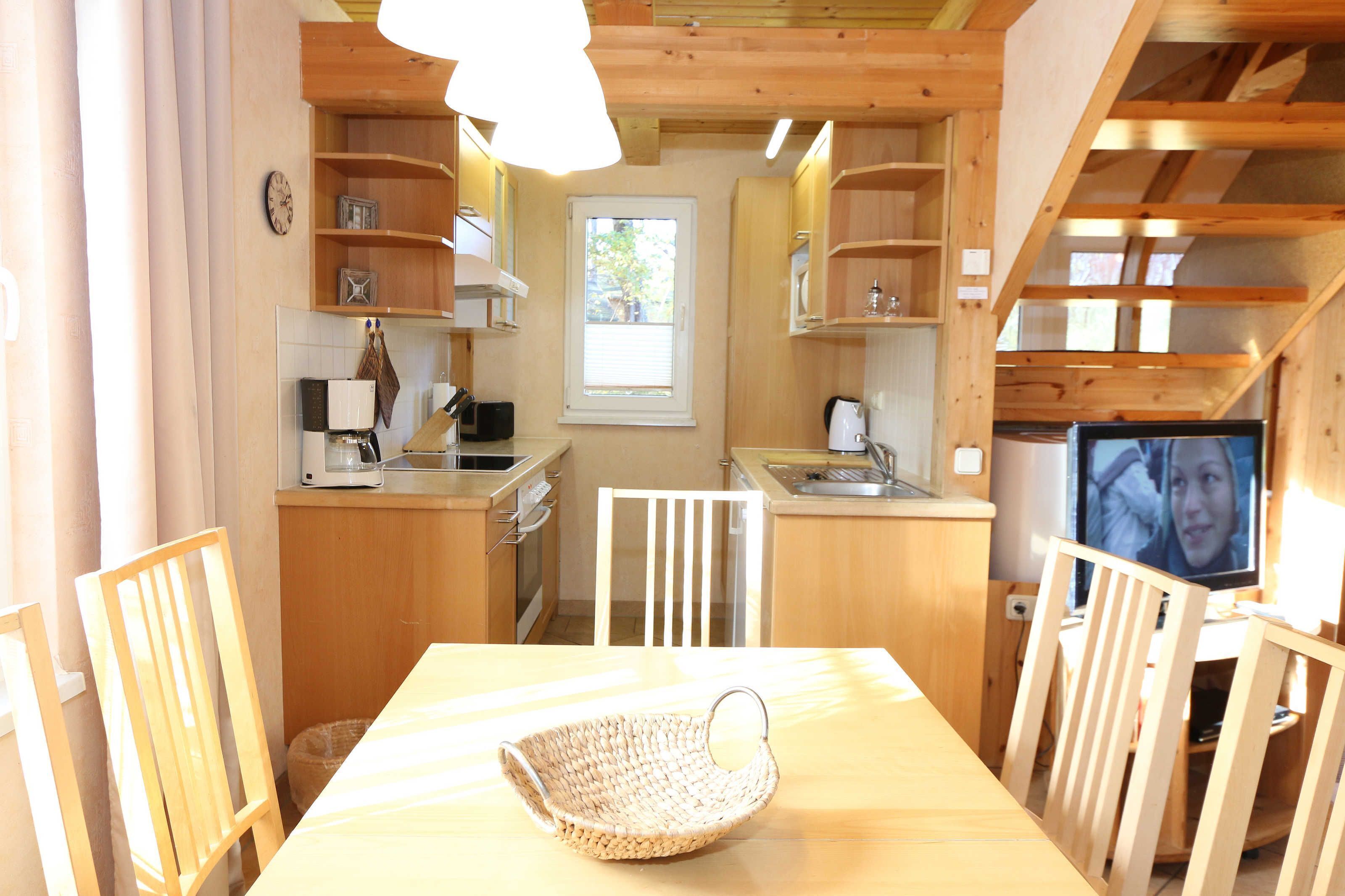 A compact kitchen with wooden cabinets, a dining table, and a television.