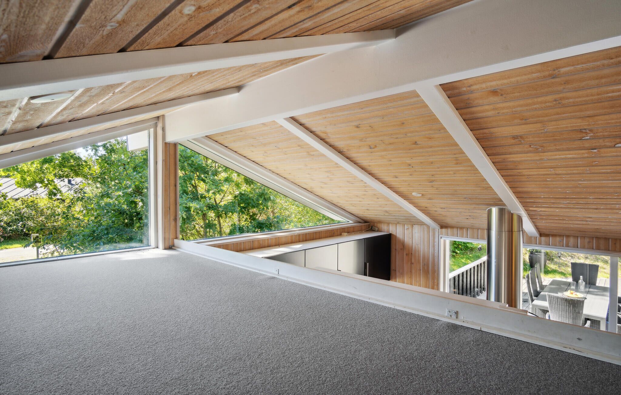 A modern interior with large windows, wooden ceiling beams, and a view of greenery outside.