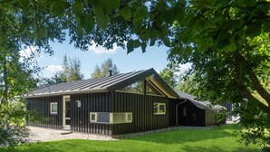 Een moderne houten chalet met een schuin dak, grote ramen en een grindpad.