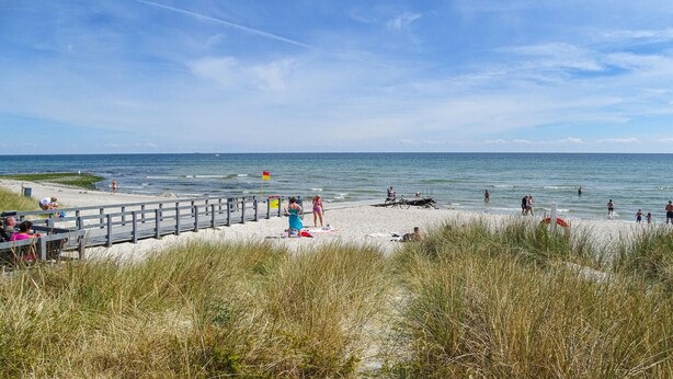 Een strand met een houten looppad, mensen die wandelen, en de oceaan op de achtergrond.