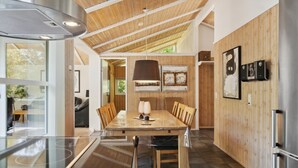 Een moderne keuken met een houten plafond, een eethoek met een grote tafel en stoelen, en uitzicht op de omgeving.