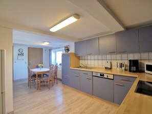 A modern kitchen with blue cabinets, a wooden dining table, and a built-in dishwasher. - Clausen: large apartment with 4 bedrooms and lounge - vacation apartment (Janneby)