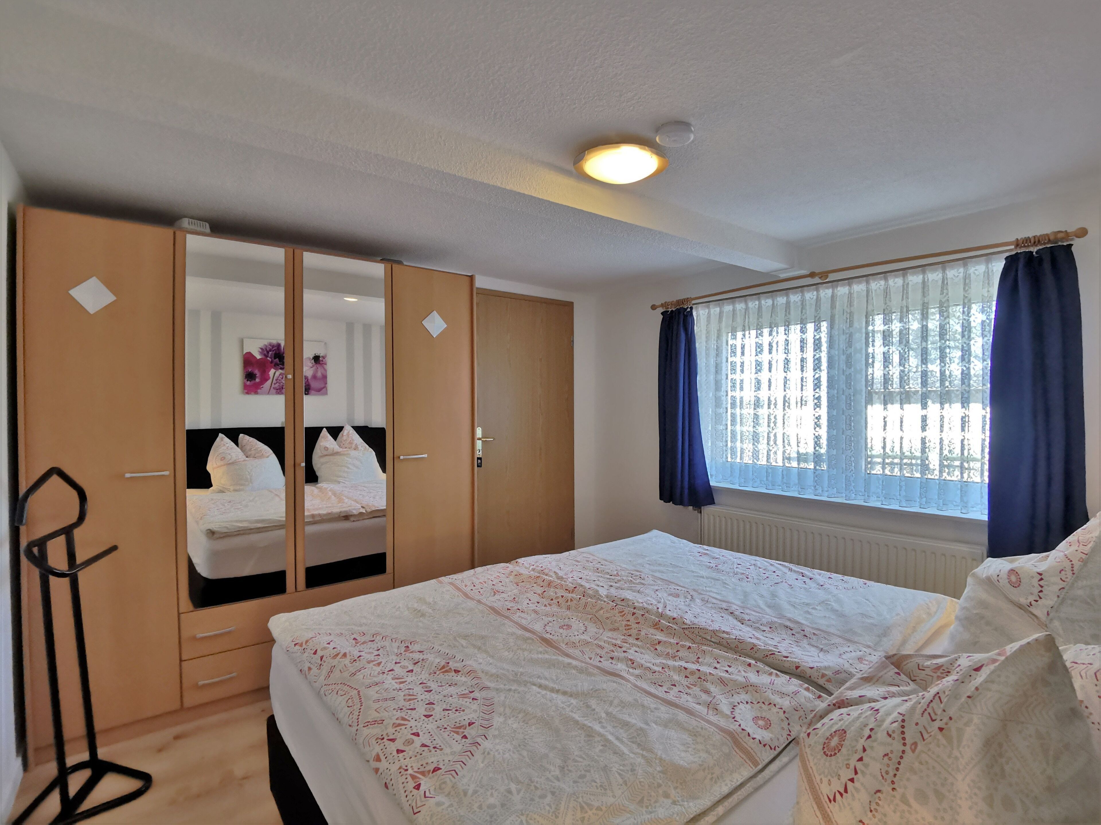 A bedroom with a bed, a wardrobe, a radiator, and a window with curtains.