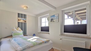 Un dormitorio con cama, una silla, ventana y radiador.