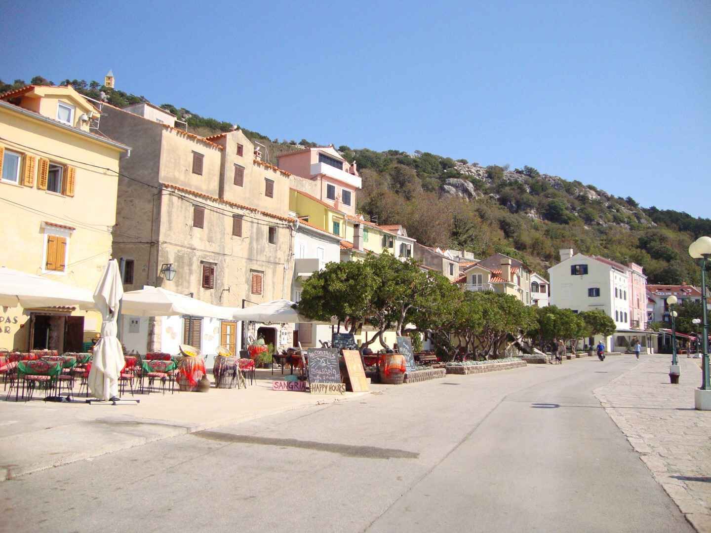 A street with buildings, outdoor seating, and a hillside in the background.