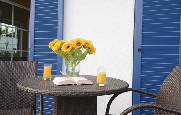 Una mesa redonda de mimbre con un libro, un jarrón de girasoles y dos vasos de jugo de naranja.
