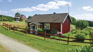 Ett litet rött trähus med ett sluttande tak, en veranda och en inhägnad trädgård.