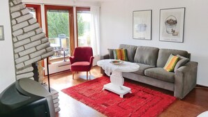 Ett vardagsrum med en röd matta, en grå soffa, en röd fåtölj och ett vitt soffbord. På väggen hänger två inramade tavlor.