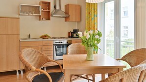 A modern kitchen with wooden cabinets, a stainless steel range hood, and a dining area with wicker chairs and a table.