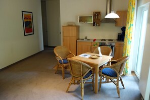 A dining area with wicker chairs and a table, a kitchen with wooden cabinets and appliances, and a framed picture on the wall.