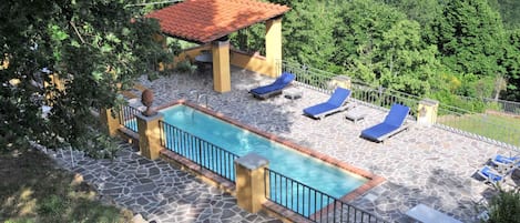 Un área de piscina con solárium empedrado, sillas de descanso y una pérgola.